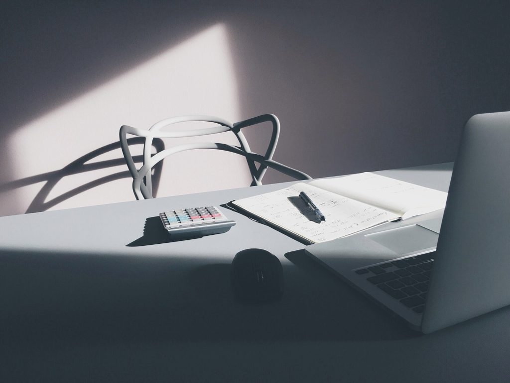 A desk with a calculator, paper notes, a pen and a laptop